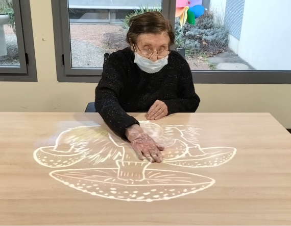 Une résidente de l'EHPAD fait du coloriage magique sur table avec la Tovertafel