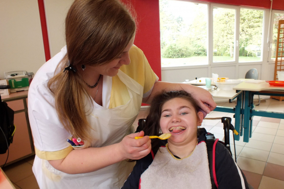 Une professionnelle du CRME aide une enfant, en fauteuil, à manger