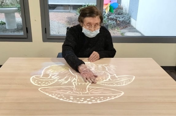 Une résidente de l'EHPAD fait du coloriage magique sur table avec la Tovertafel